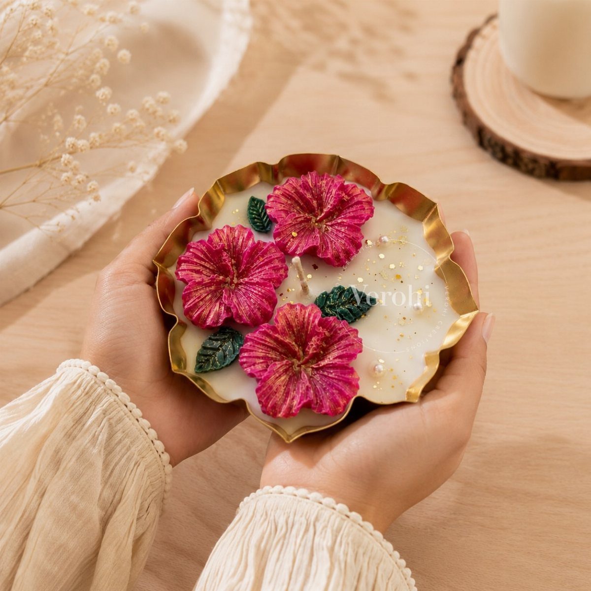 Hands holding a decorative white candle with pink wax flowers in a gold holder.