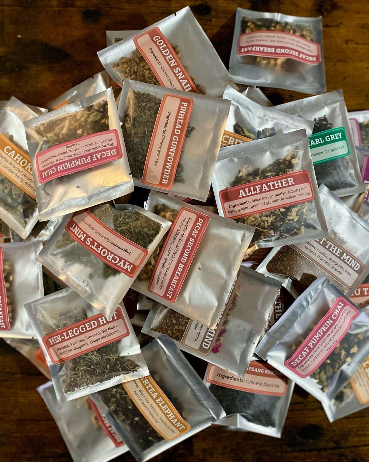 Small clear packets of loose leaf tea samples with colorful labels on wood.