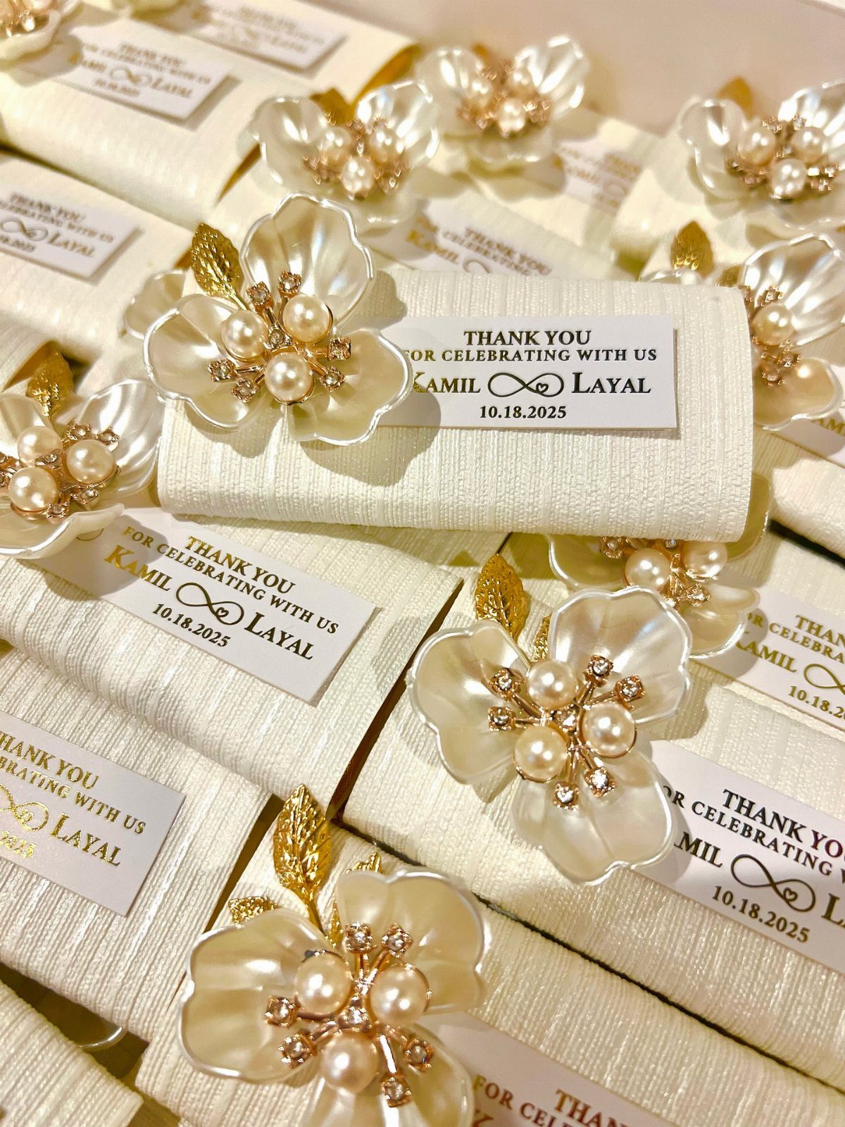 White fabric-wrapped party favors with pearl floral brooches and thank-you tags.