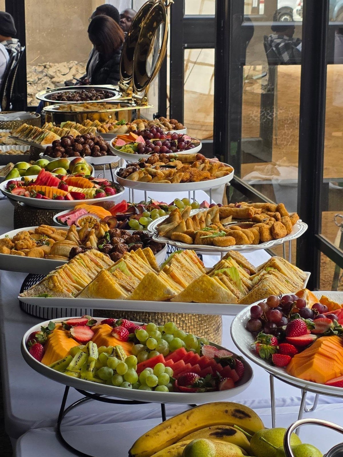 Buffet table with platters of sandwiches, pastries, and fresh fruit for a party.