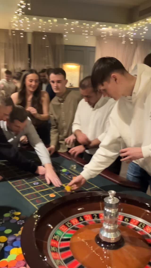 Young adults playing at a casino table with a roulette wheel and chips.