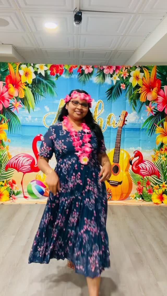Woman in floral dress and lei posing before a tropical beach party backdrop.