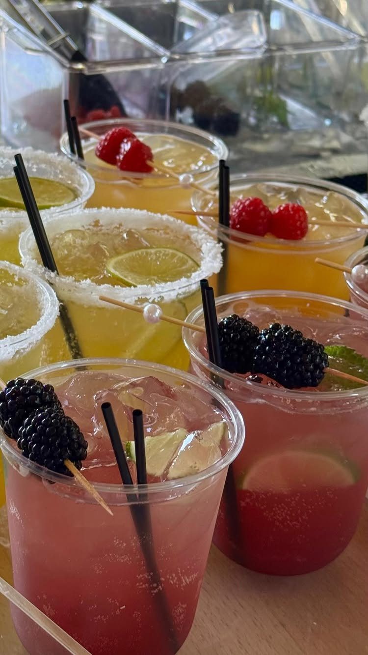 Colorful iced beverages in plastic cups garnished with fresh berries and lime slices.