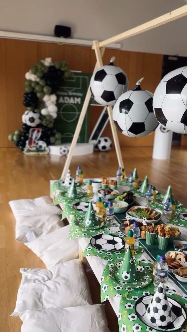 Soccer themed party table with green decor, soccer ball plates, and large balloons.