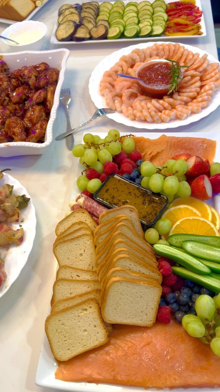 Assorted party platters with shrimp, smoked salmon, fresh fruit, and vegetables on a table.