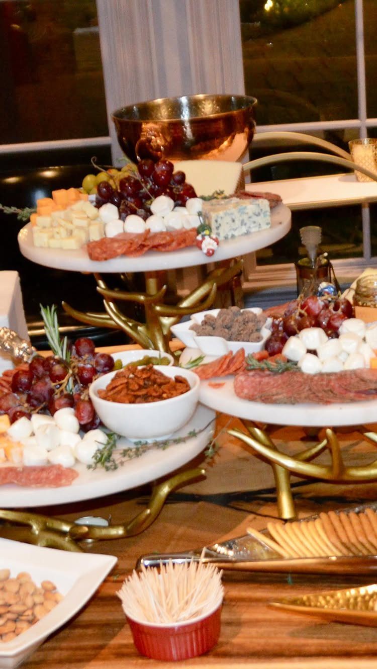 Gourmet appetizer platters with cheeses, meats, and grapes on gold stands.