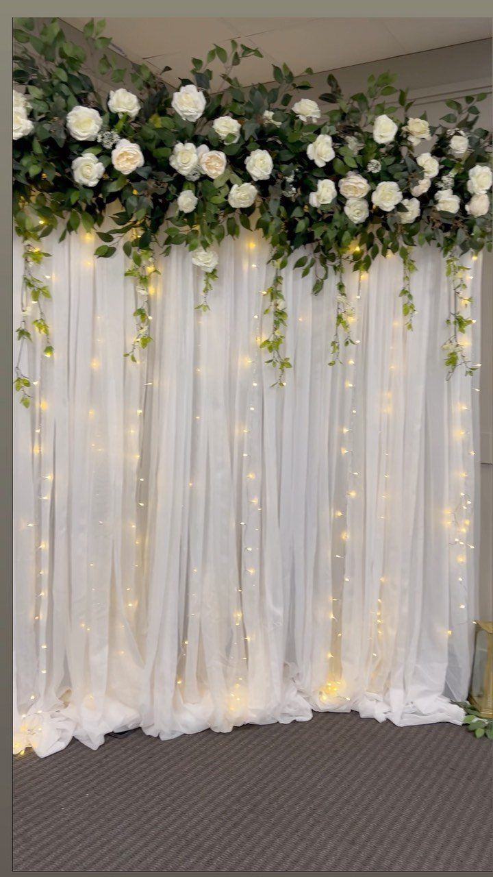 White sheer curtain backdrop with fairy lights and white rose floral garland top