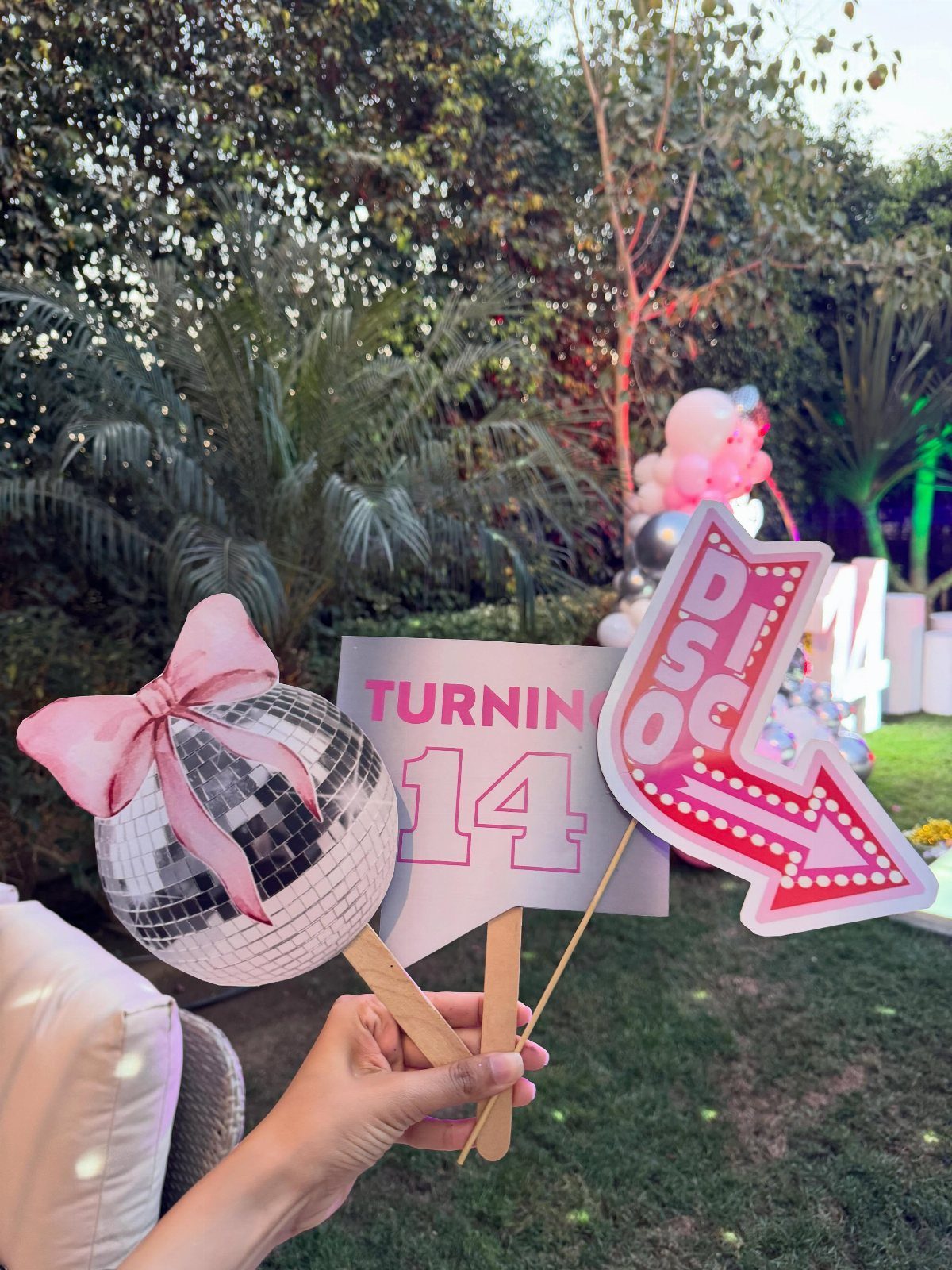 Hand holding disco ball, turning 14 sign, and pink arrow photo booth props