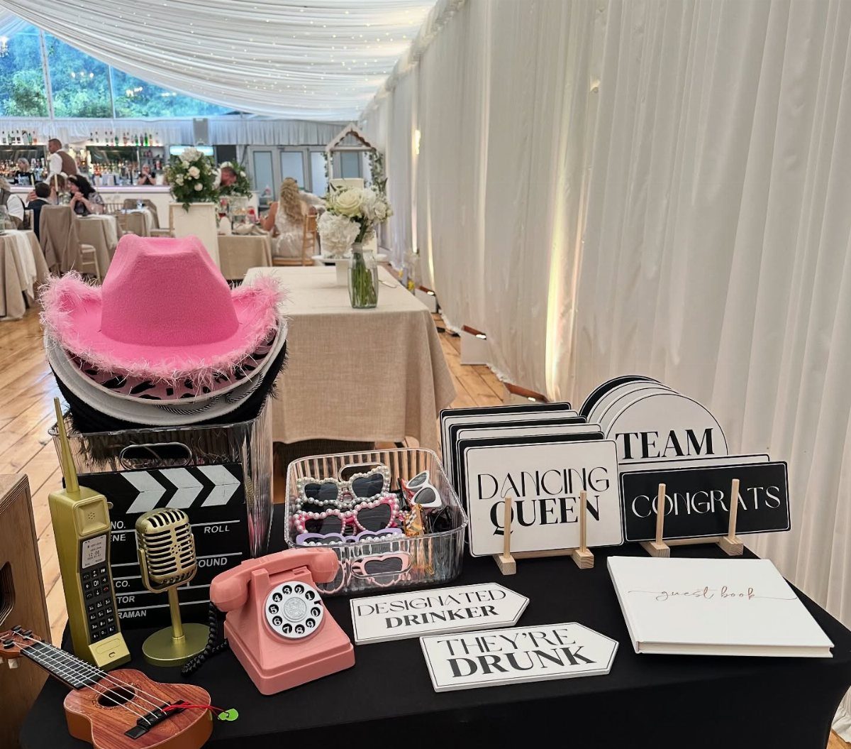 Photo booth props including a pink cowboy hat and signs on a table.