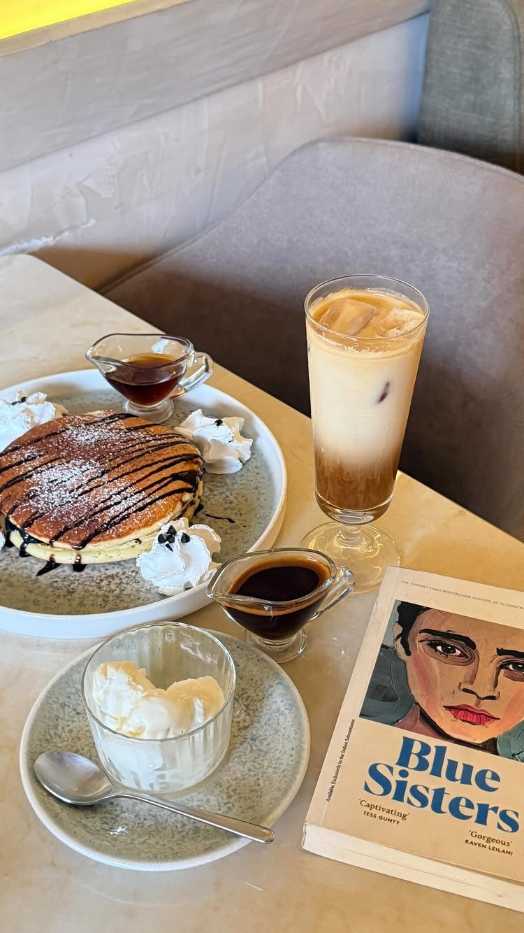 Iced latte, chocolate pancakes, and a book on a light cafe table.