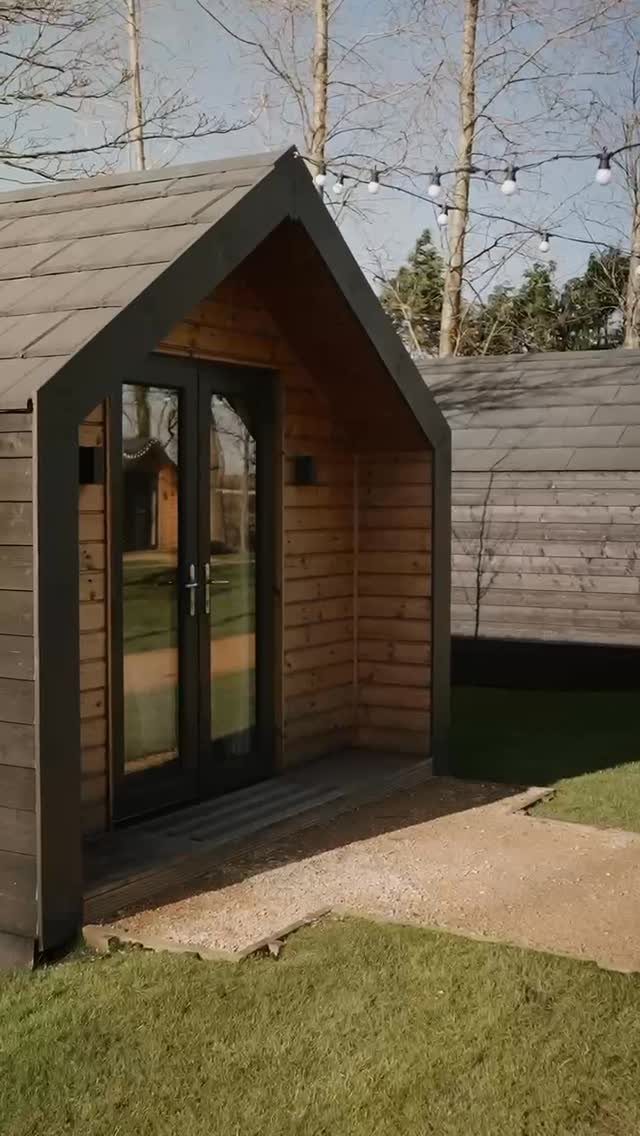 Modern wooden cabin with glass doors on a lawn under string lights.