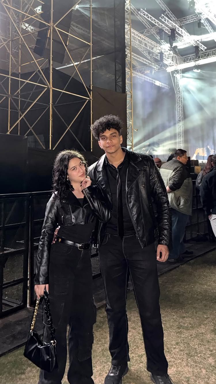 Young couple in black leather jackets posing in front of a concert stage.