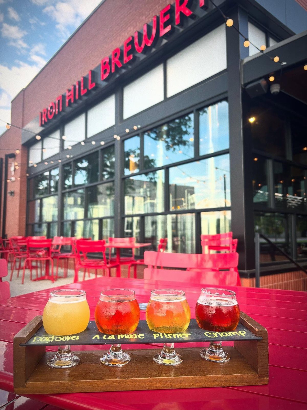 Beer flight on a red table in front of Iron Hill Brewery building