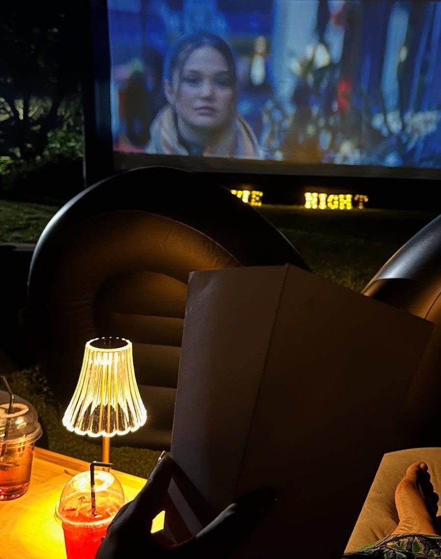 Outdoor movie screen showing a film with beanbag seating and snacks at night.