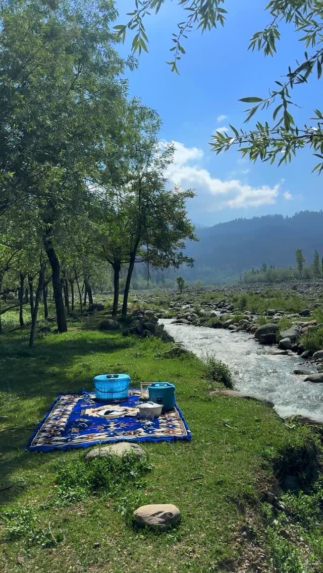 Picnic blanket and food by a river with mountains in the background