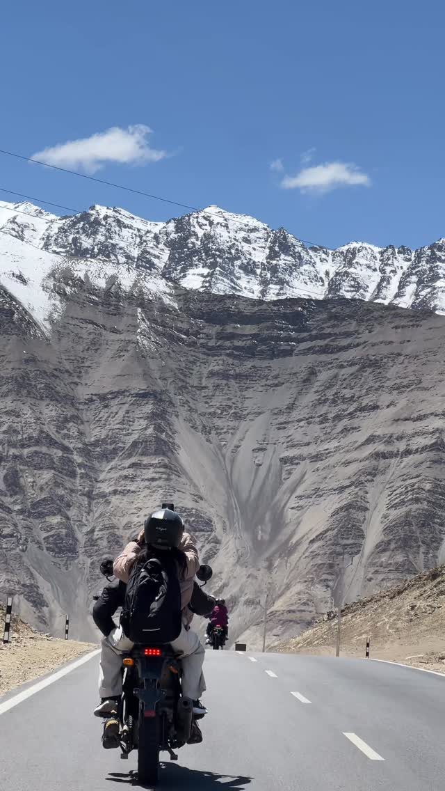 Couple on a motorcycle riding toward snow-capped mountains on a paved road
