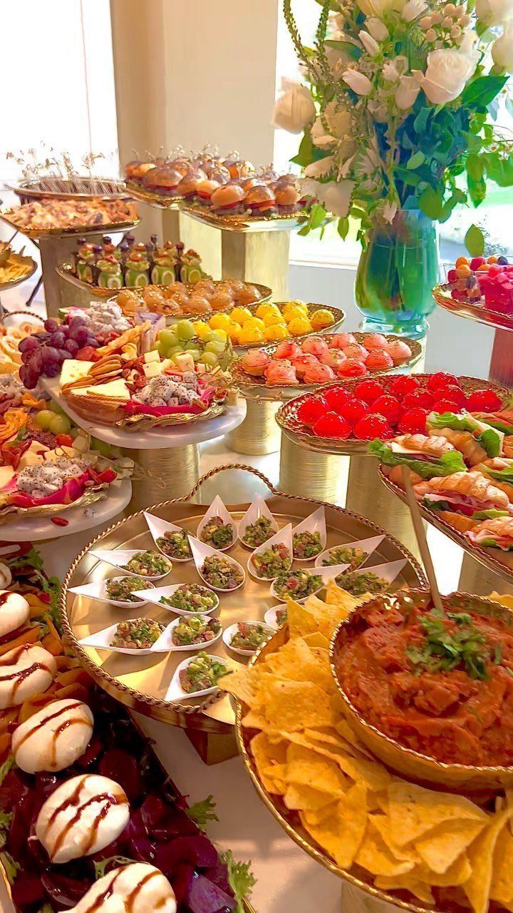 Lavish buffet spread with fruit, appetizers, and dips on gold platters with flowers.