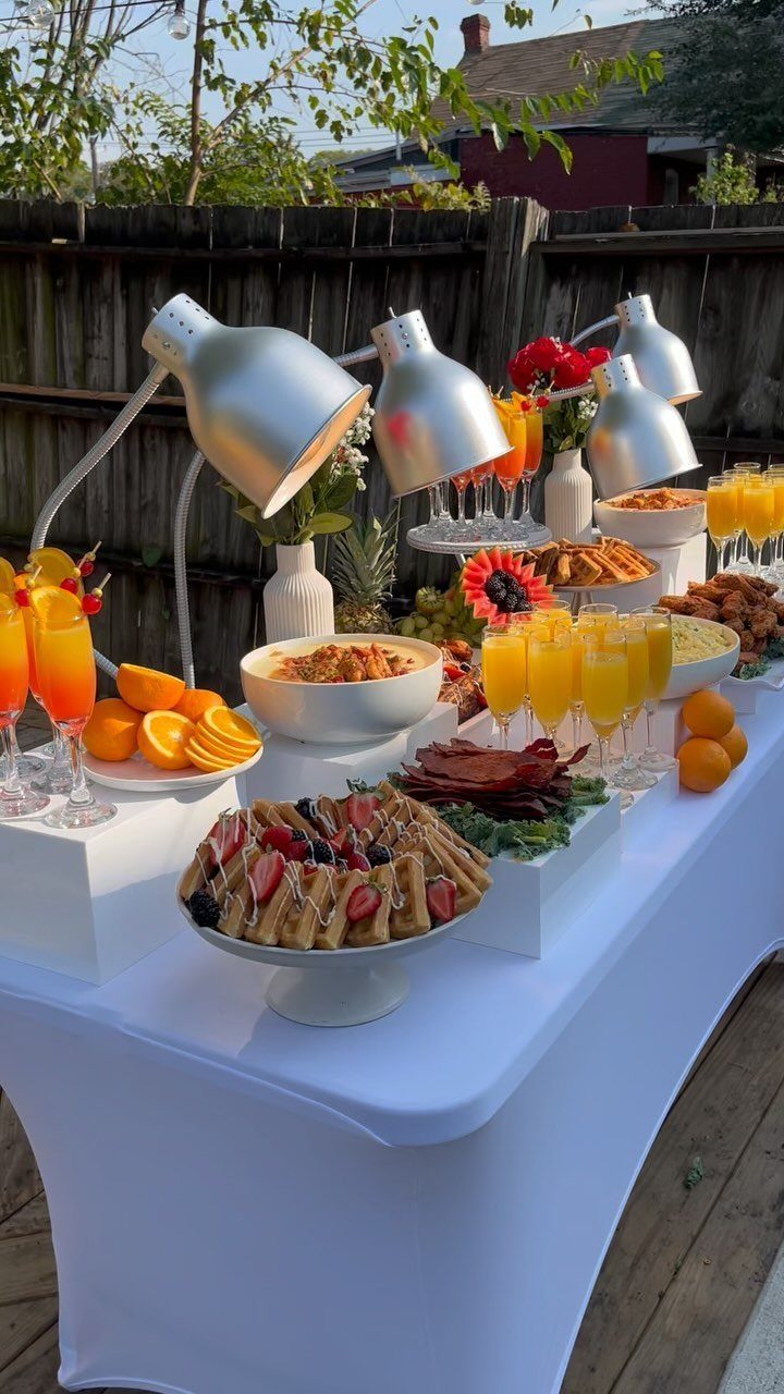 Buffet table with waffles, orange mimosas, and fresh fruit for a brunch party.