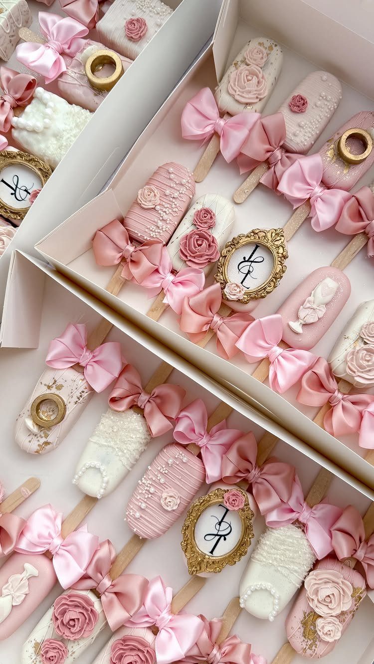Decorated pink and white cake pops with frosting roses and gold rings in boxes.