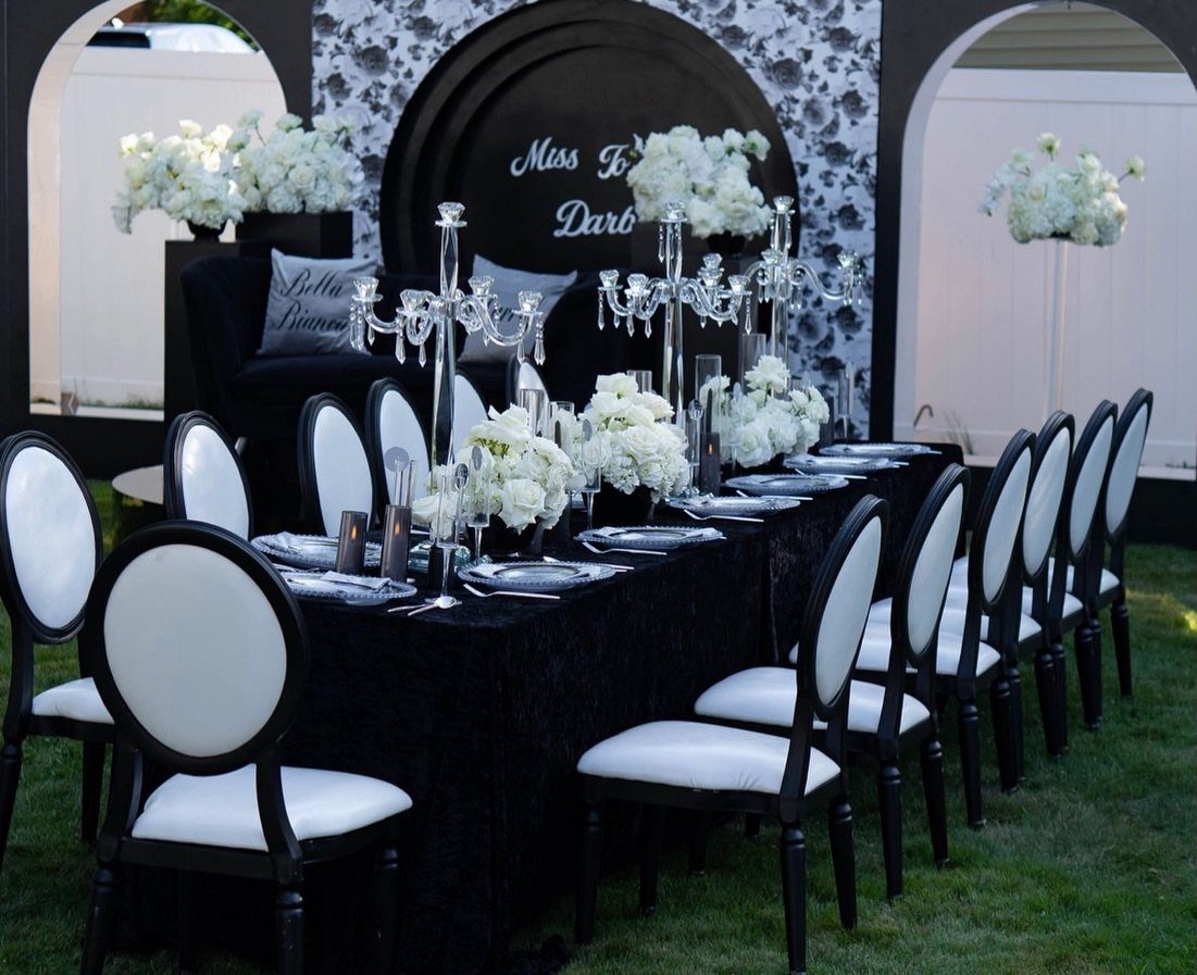 Elegant black and white dinner table setting with white flowers and crystal candelabras outdoors.
