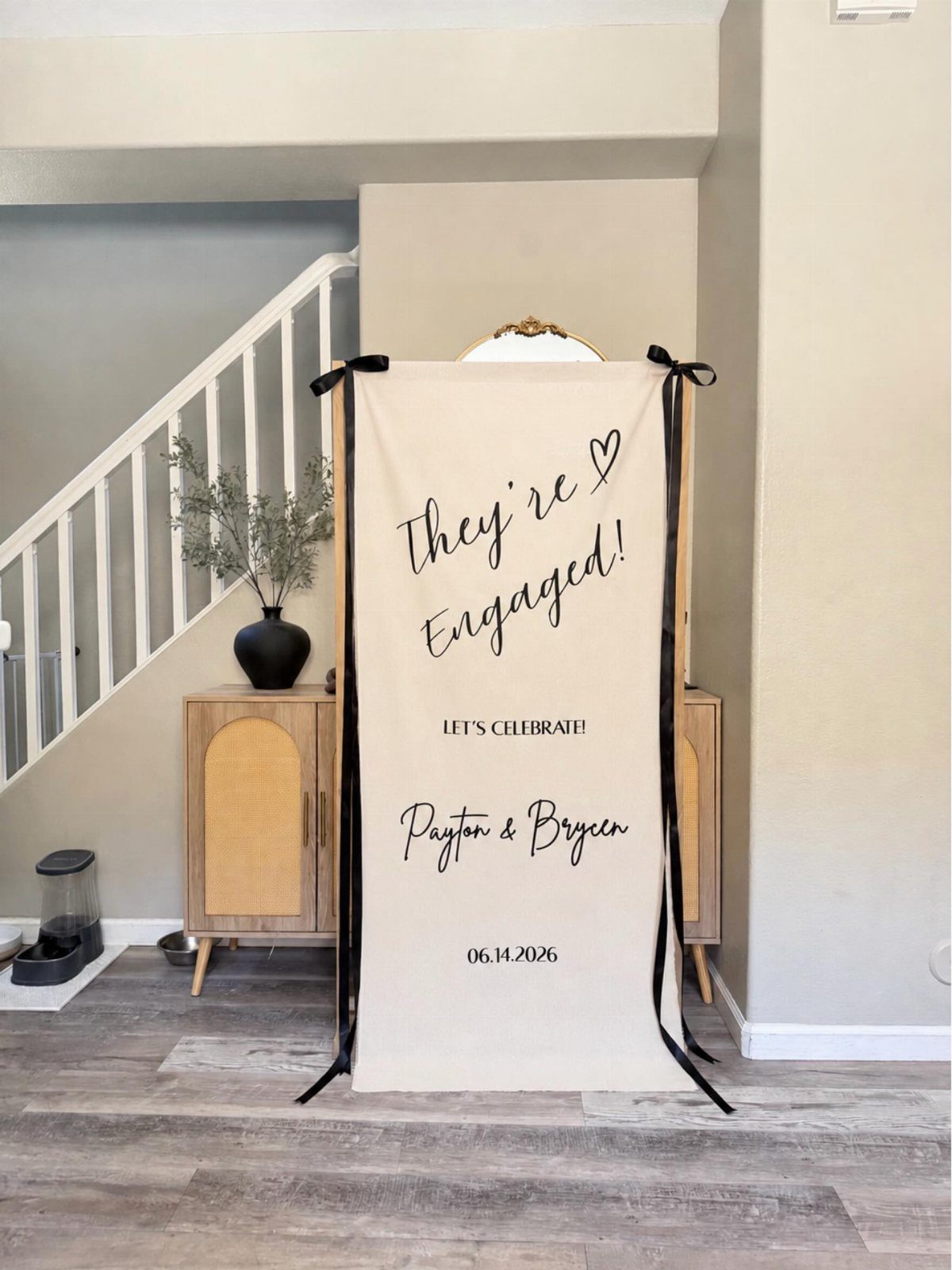 Beige engagement party banner with black text standing in a modern home interior.