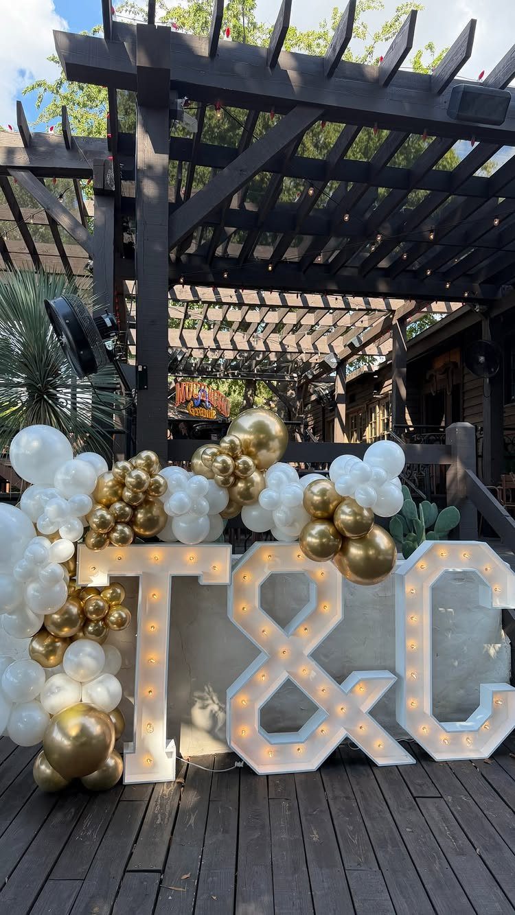 Large illuminated T & G marquee letters surrounded by white and gold balloons.