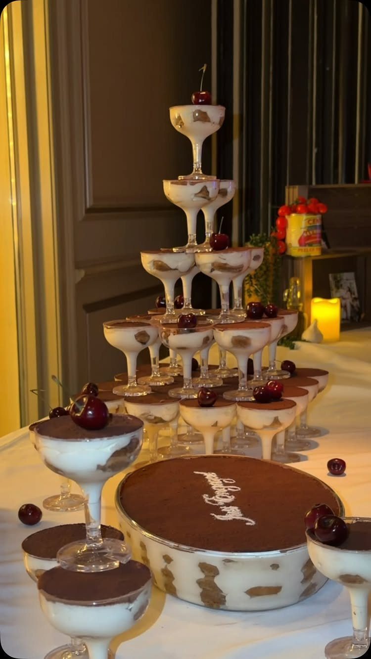 Dessert tower of cream glasses and a cocoa-topped cake on a white table.