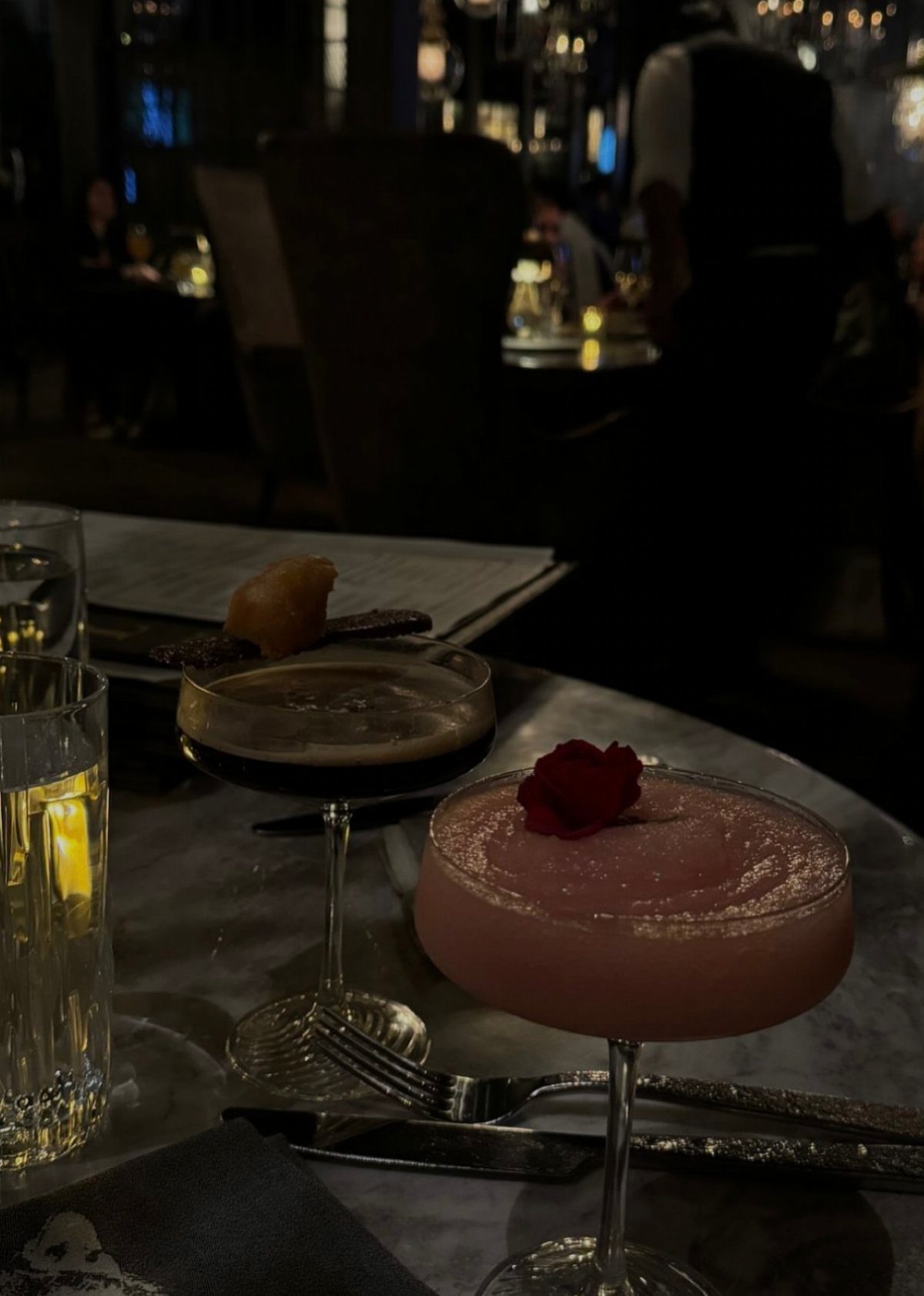 Two elegant cocktails, one pink with a rose petal, on a marble table.