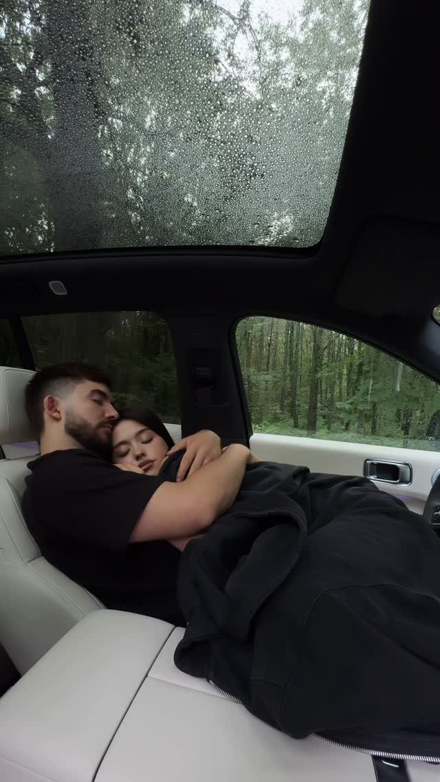 Couple cuddling under a blanket in a car with a rainy sunroof and forest view