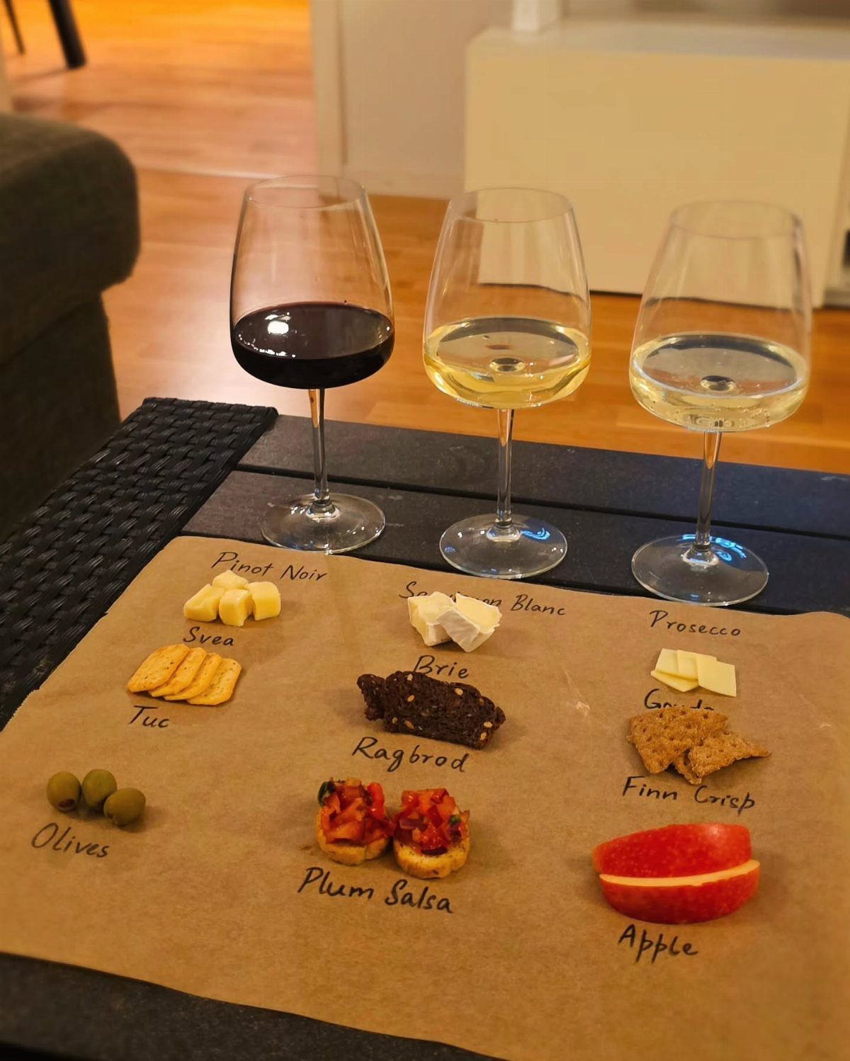 Three glasses of red and white wine with labeled cheese and fruit pairings.