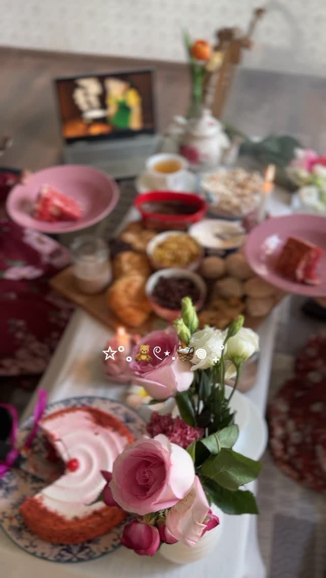 Indoor picnic spread with pink cakes, pastries, and roses on a white cloth.