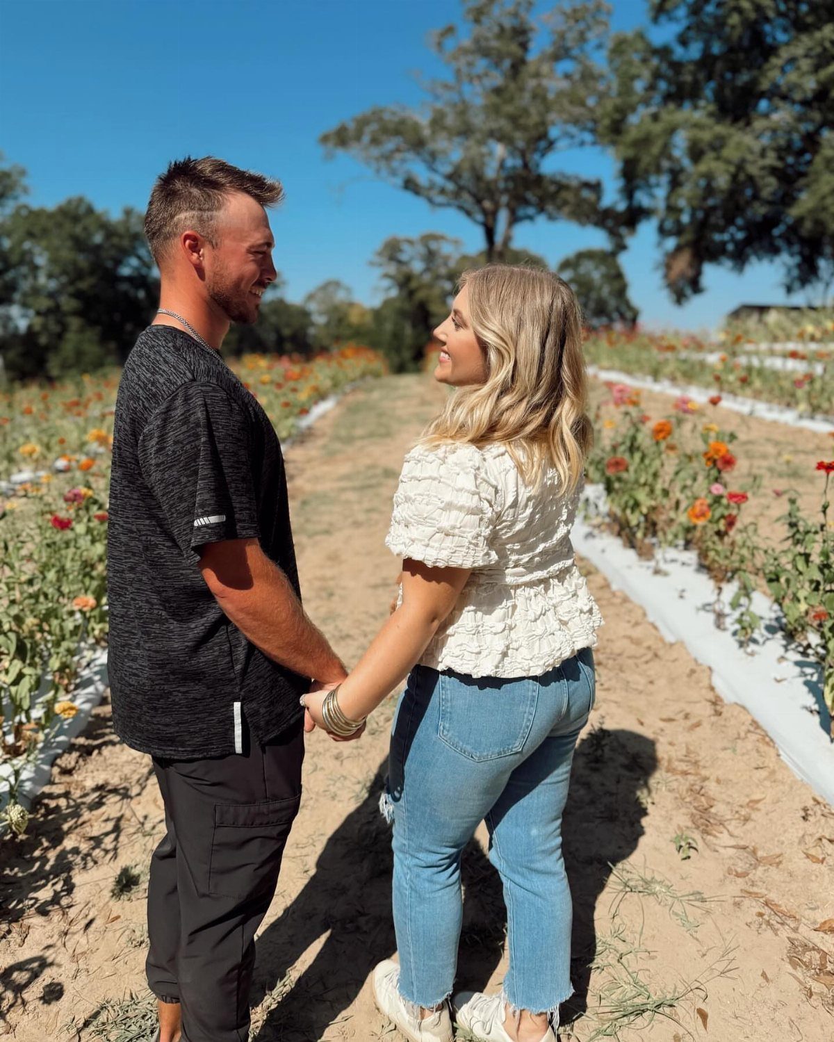 Couple holding hands and smiling in a field of orange flowers under blue sky