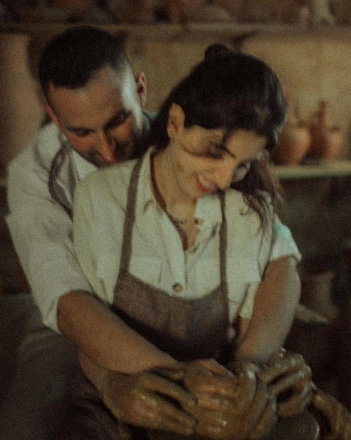 Couple in aprons shaping clay together on a pottery wheel in a studio