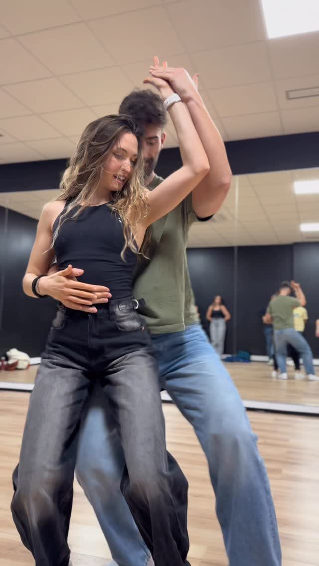 Couple dancing together in a studio with mirrors and wooden floors.