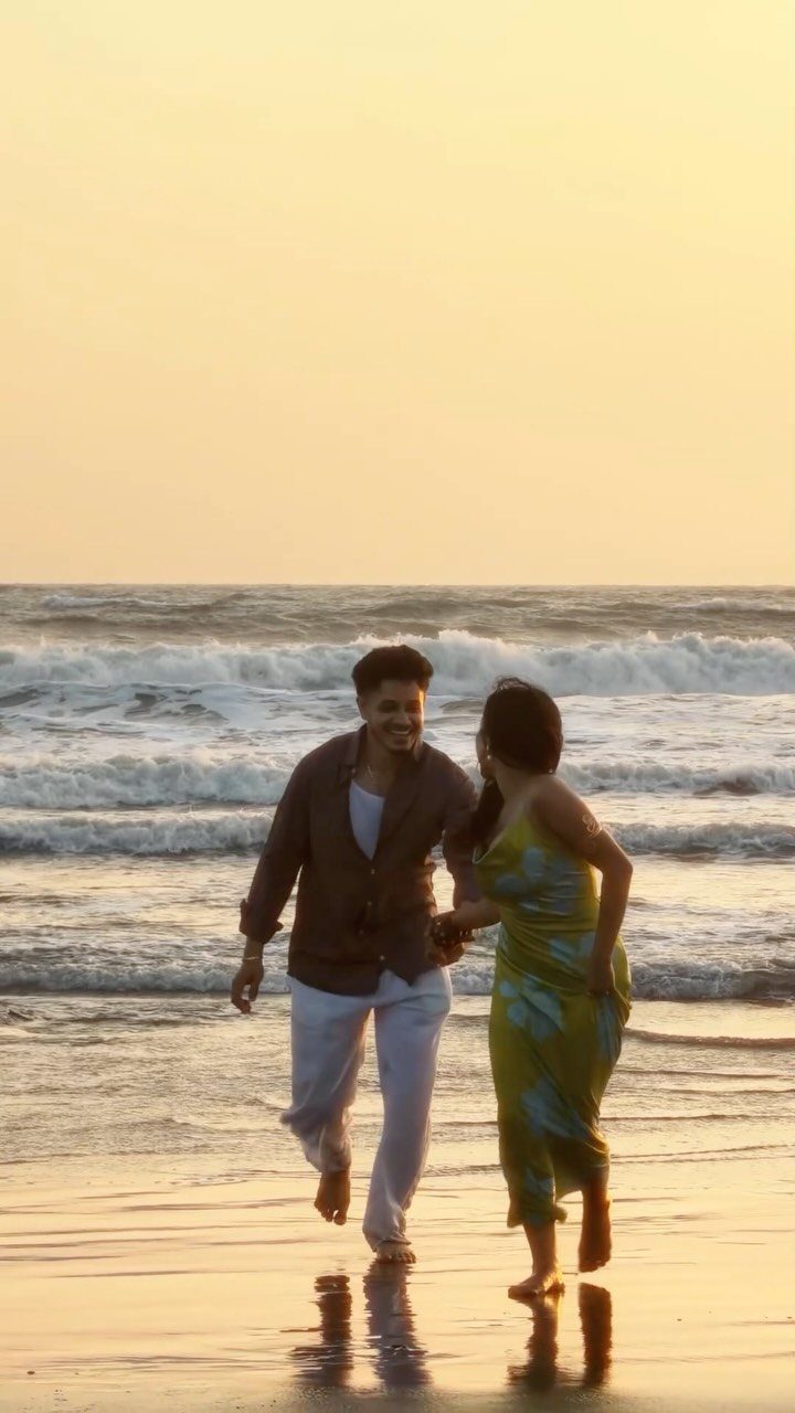 Couple holding hands and walking on a beach during a golden sunset.