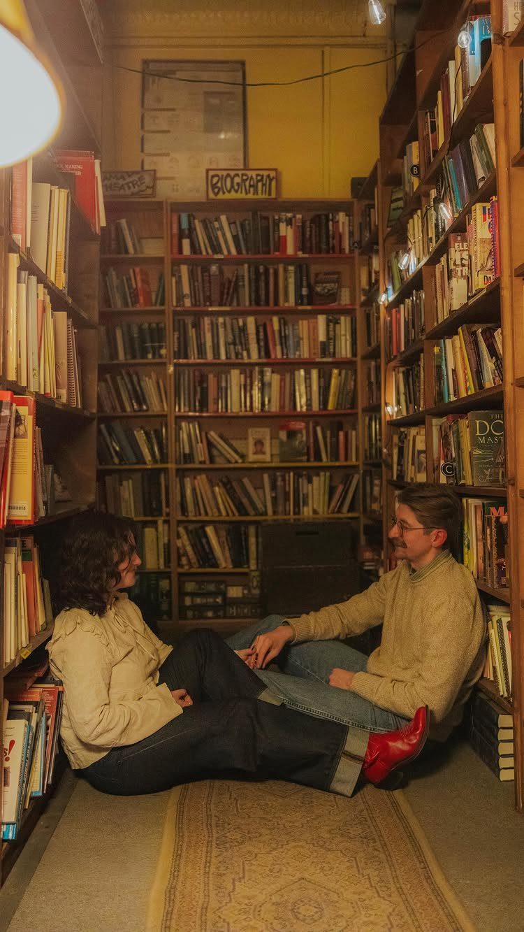 Couple sitting on a rug between bookshelves in a cozy bookstore talking together.