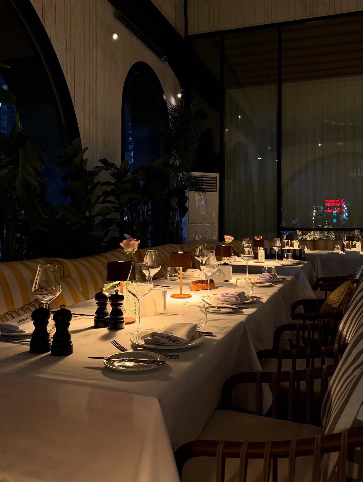 Elegant restaurant table setting with white linens, wine glasses, and a single pink rose.