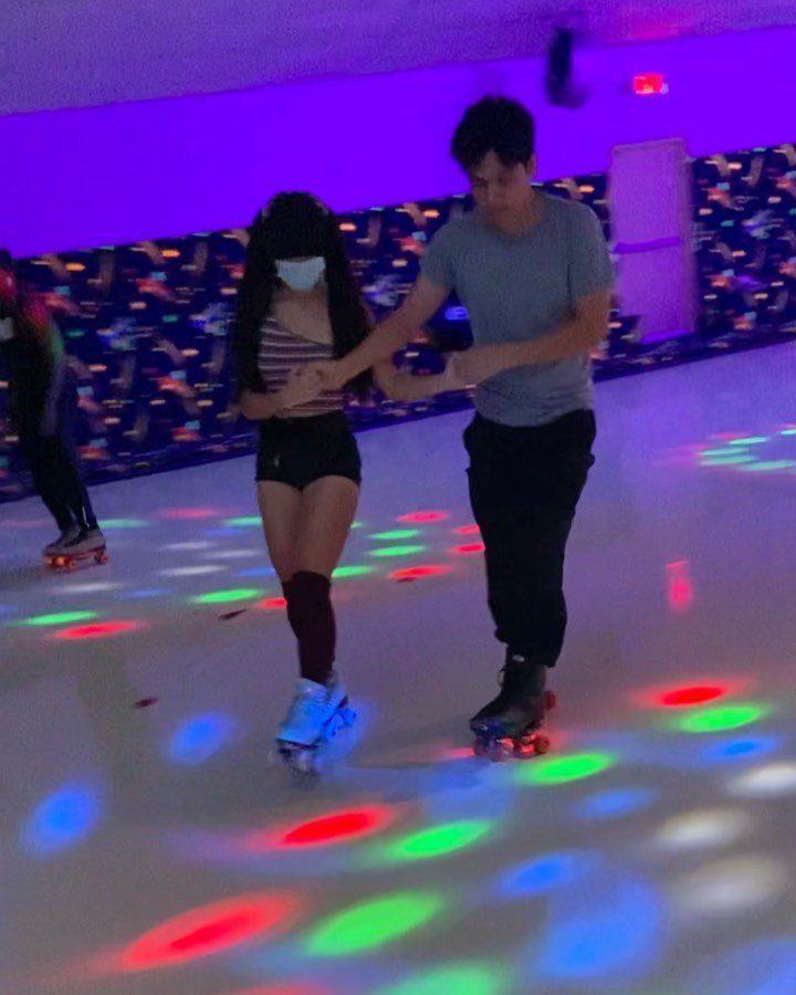 Couple holding hands while roller skating in a rink with colorful light projections.