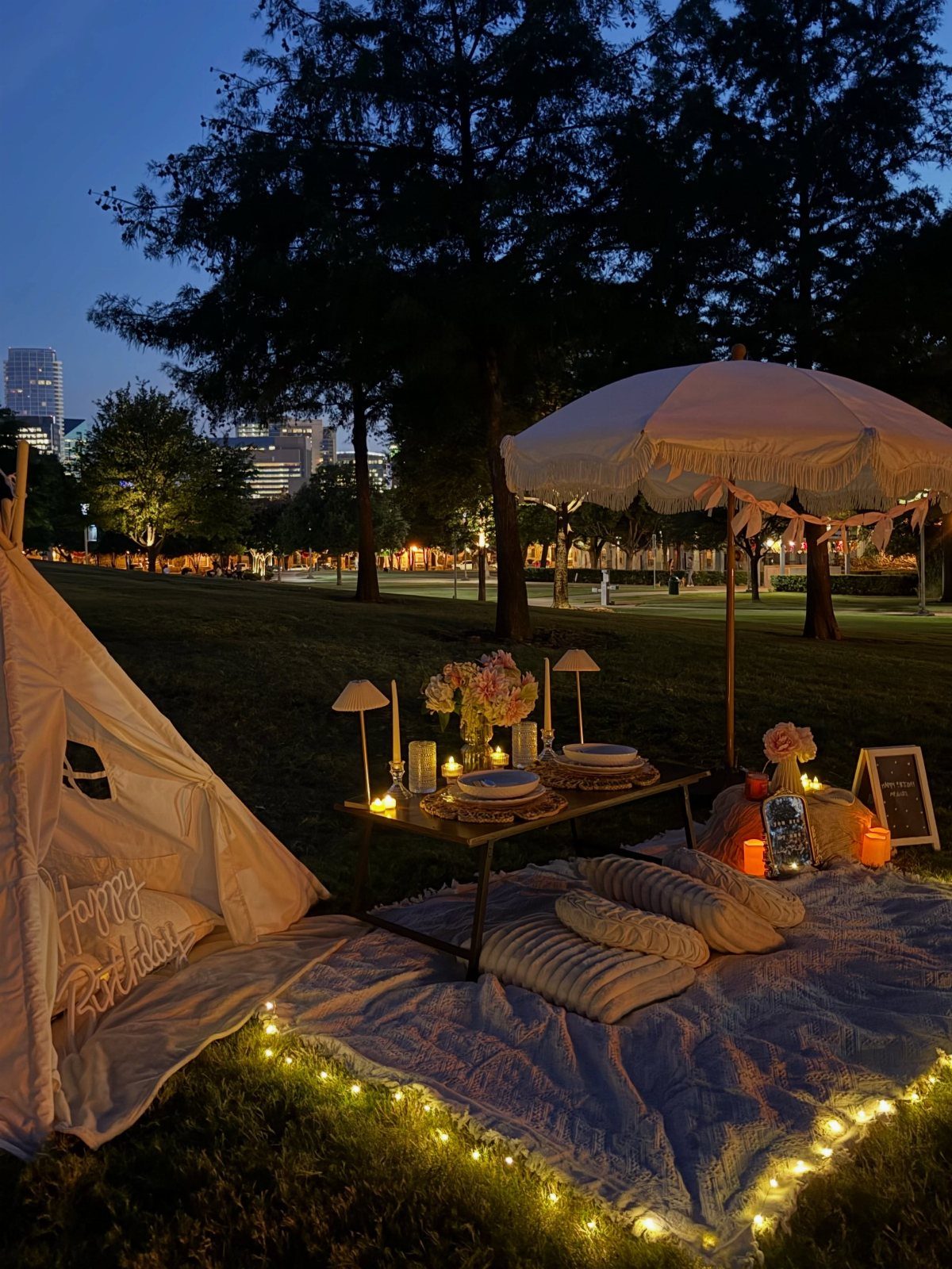 Romantic outdoor picnic setup with a low table, white umbrella, and fairy lights.
