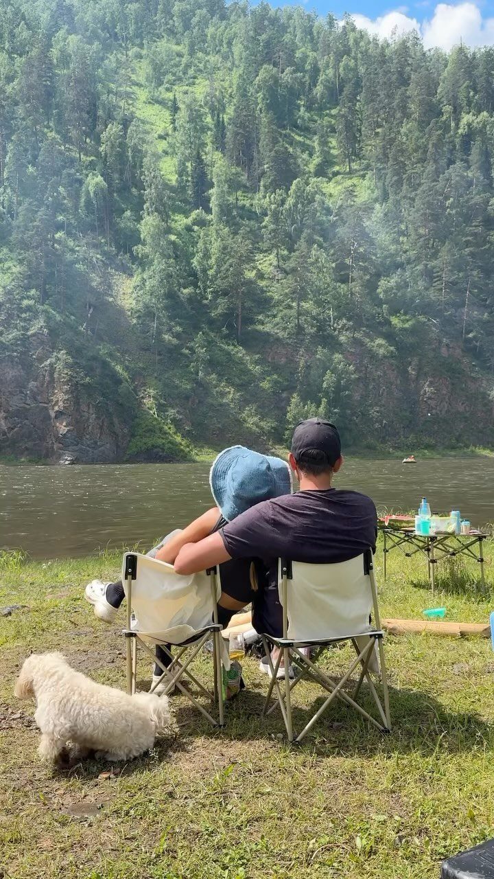 Couple sitting in folding chairs by a river with a forested mountain background