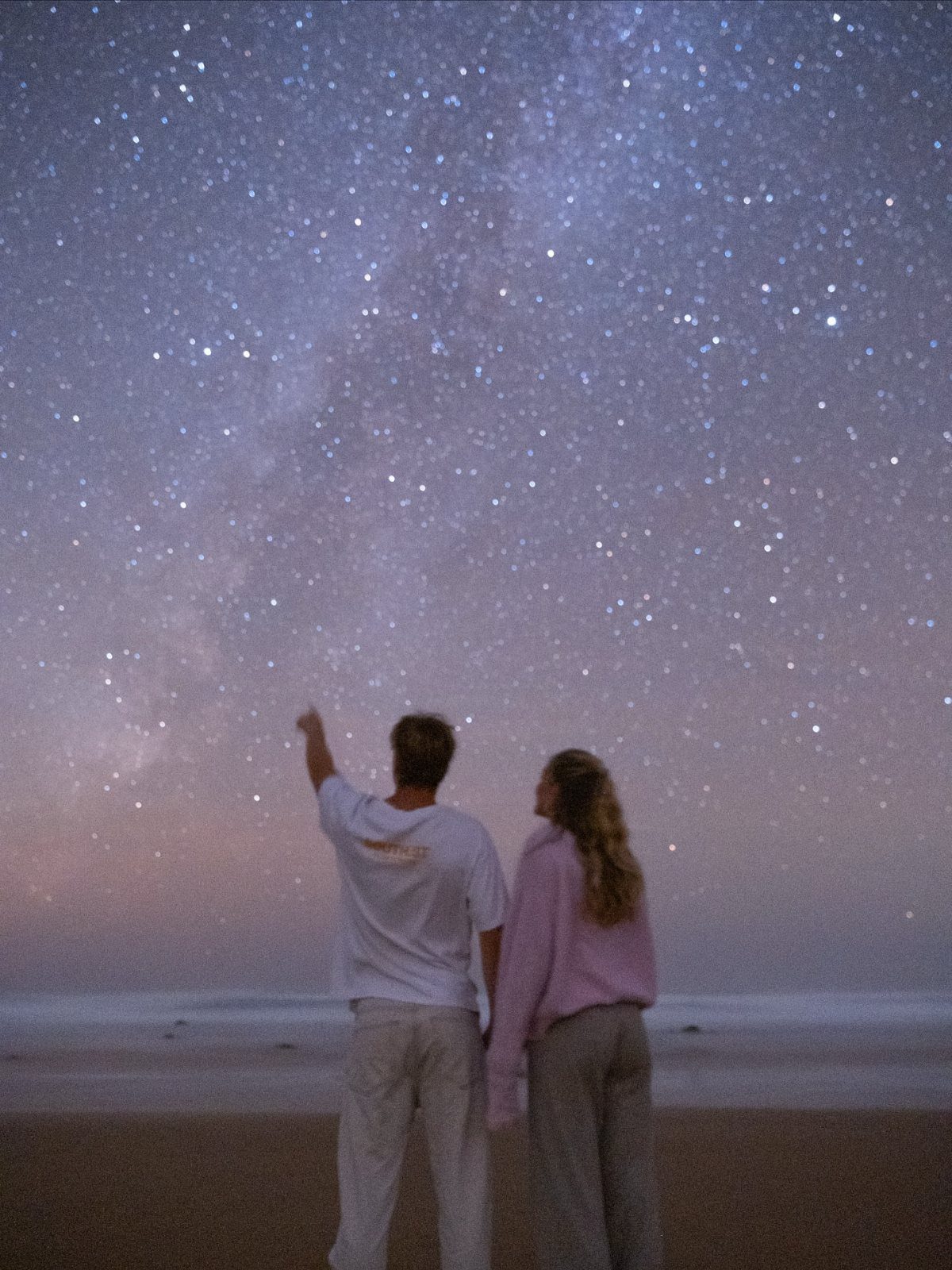Couple standing on a beach at night looking up at a starry sky