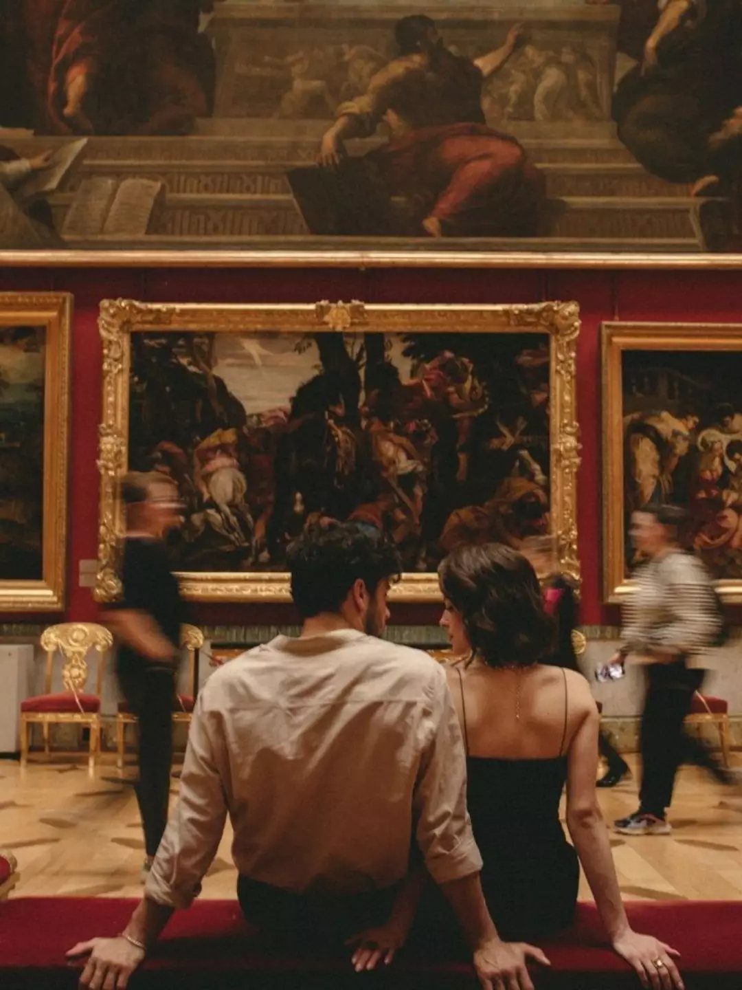 Couple sitting together in an art gallery looking at large gold-framed paintings