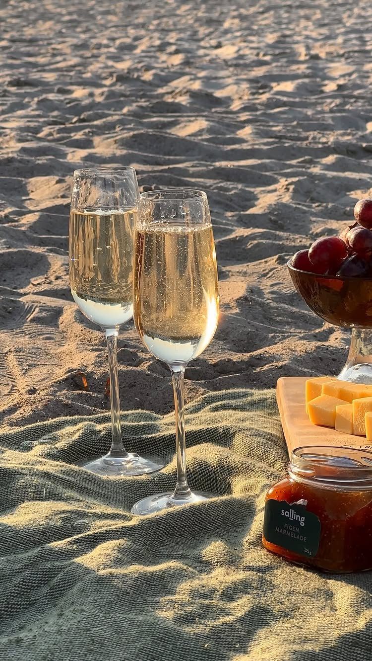 Two glasses of champagne and snacks on a blanket over beach sand.