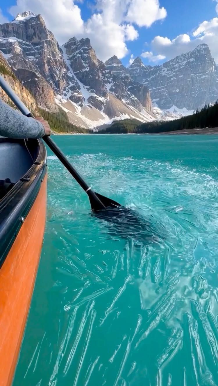 Person paddling an orange canoe through turquoise water with mountains in the background