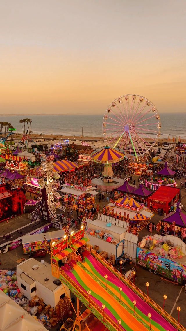 Colorful carnival on a beach with a Ferris wheel and carousel at sunset.