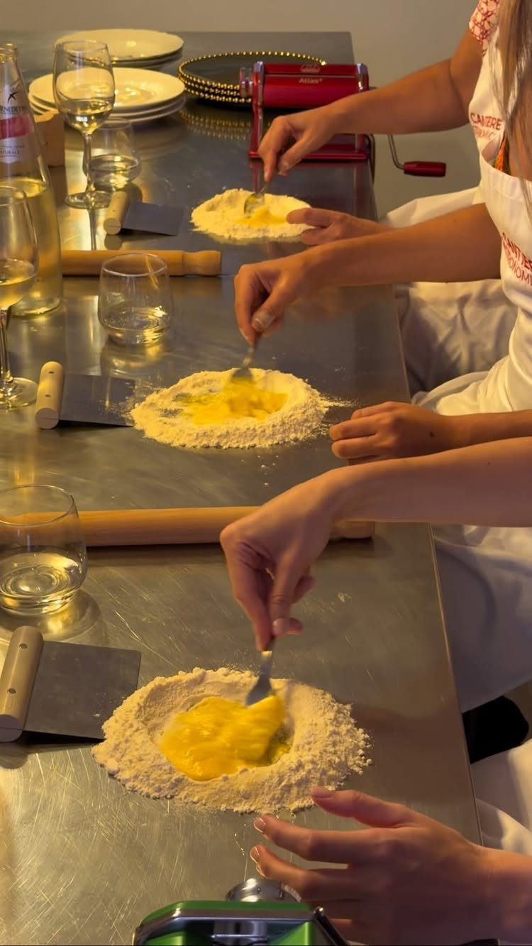 People in white aprons making fresh pasta with flour and eggs at a counter