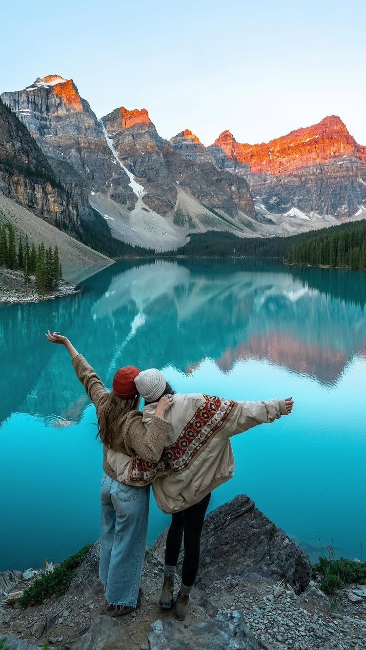 Two women standing on a rocky cliff overlooking a turquoise mountain lake