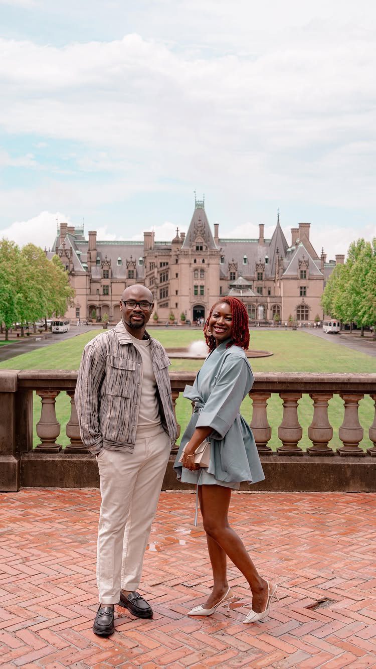 Couple posing on a brick terrace in front of the Biltmore Estate chateau.