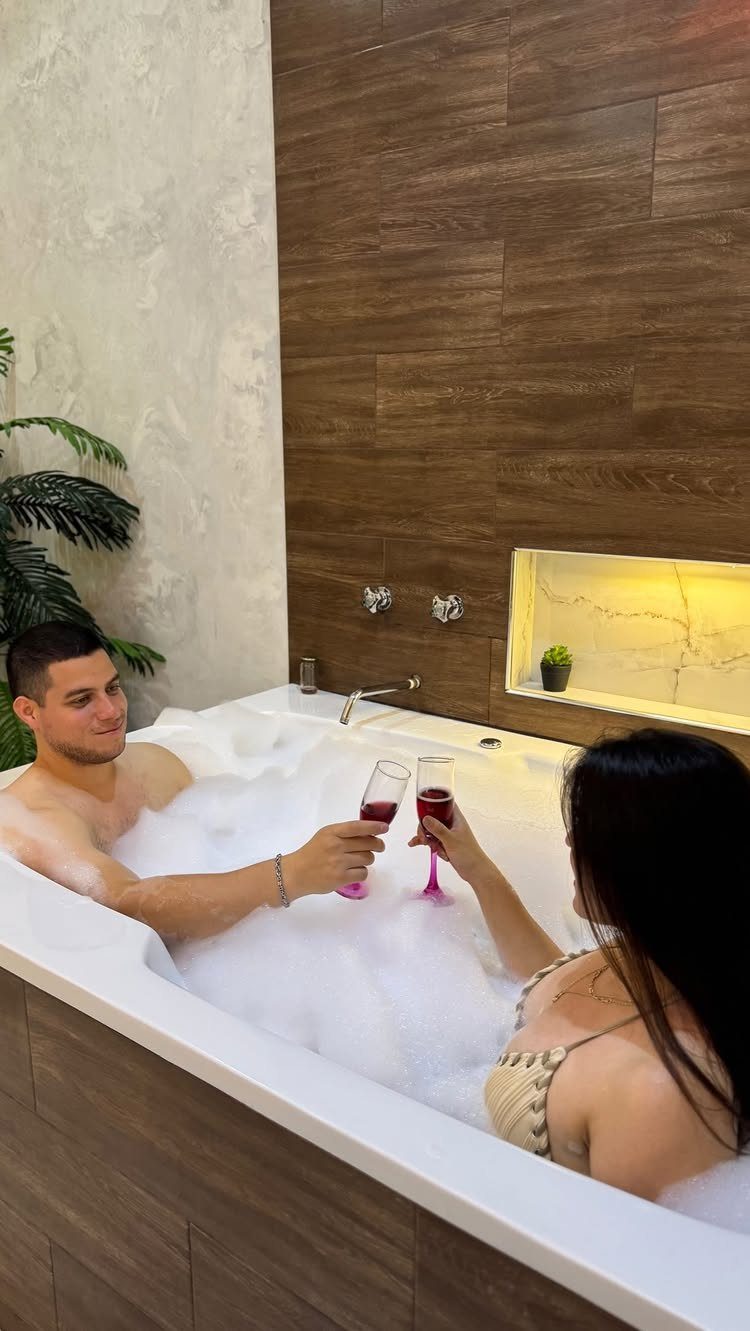 Couple clinking champagne glasses while relaxing in a bubble bath in a modern bathroom