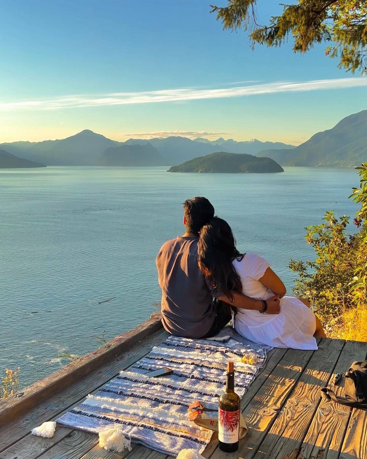 Couple sitting on a wooden deck overlooking a mountain lake with wine.